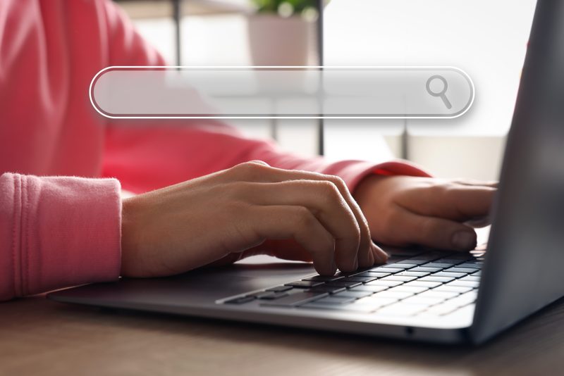 Hands typing on a laptop with a search bar overlay